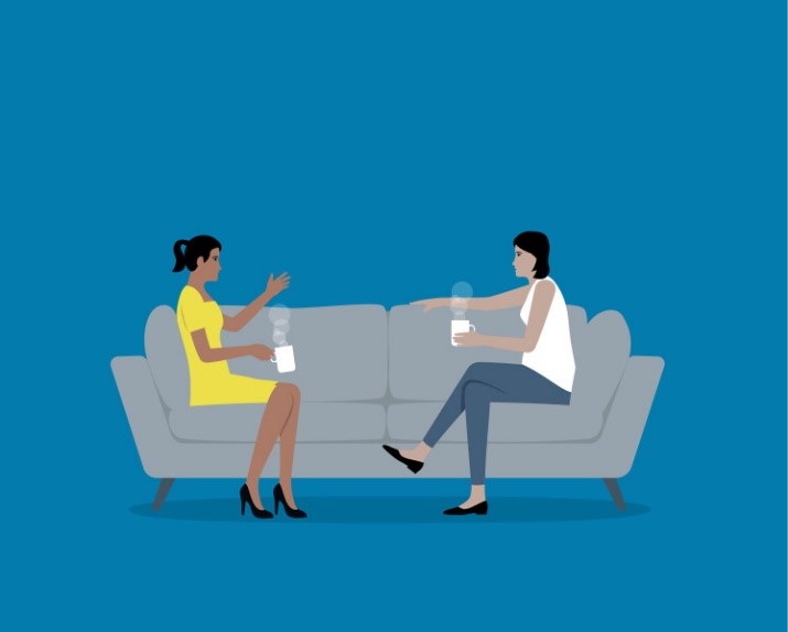 Two women having a conversation on couch with coffee